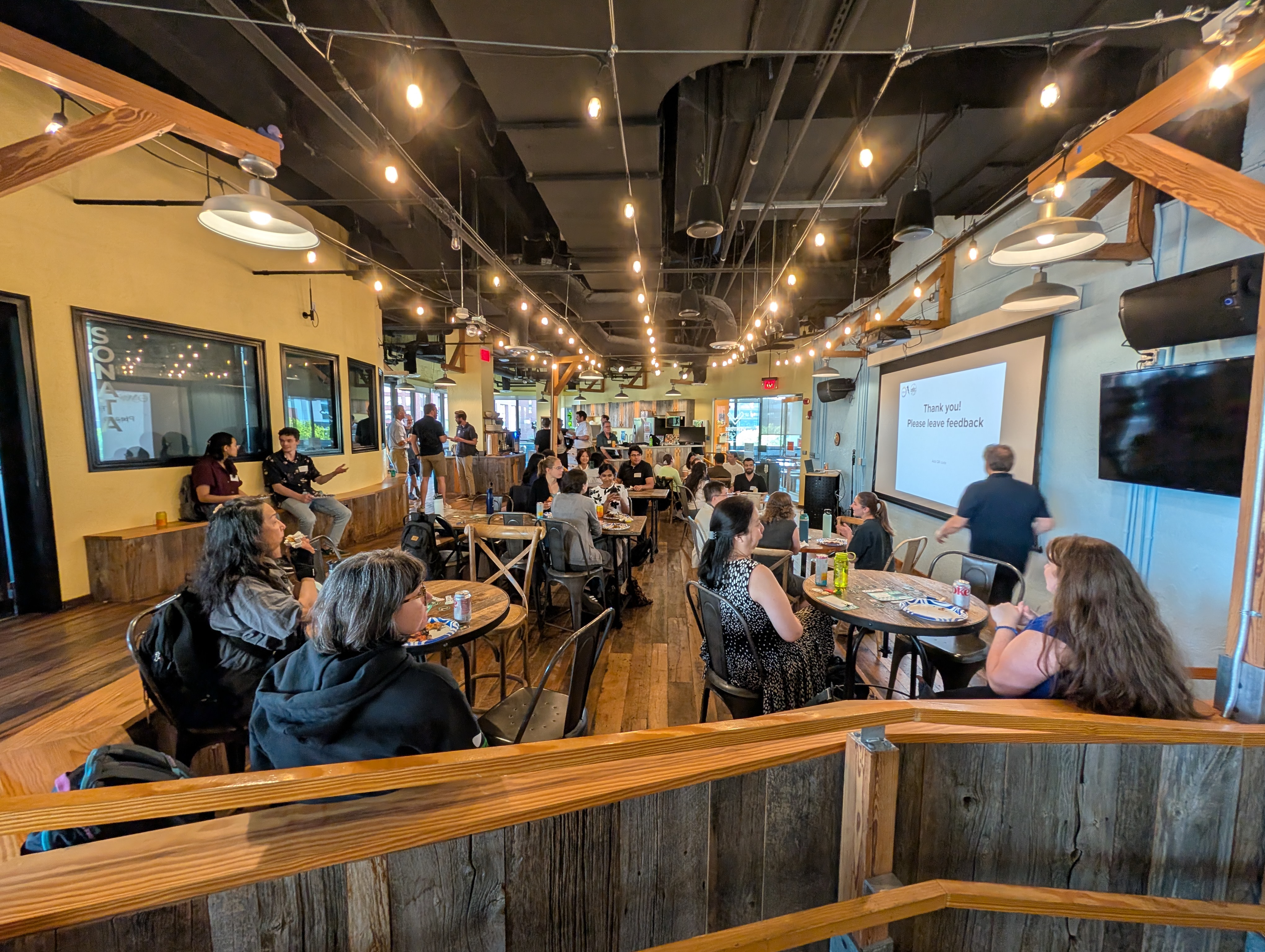 A photo of a crowded, vibrant event space at the CIC. A large, engaged audience of professionals is seated and standing around small tables, looking toward the main stage in anticipation of the next speaker.